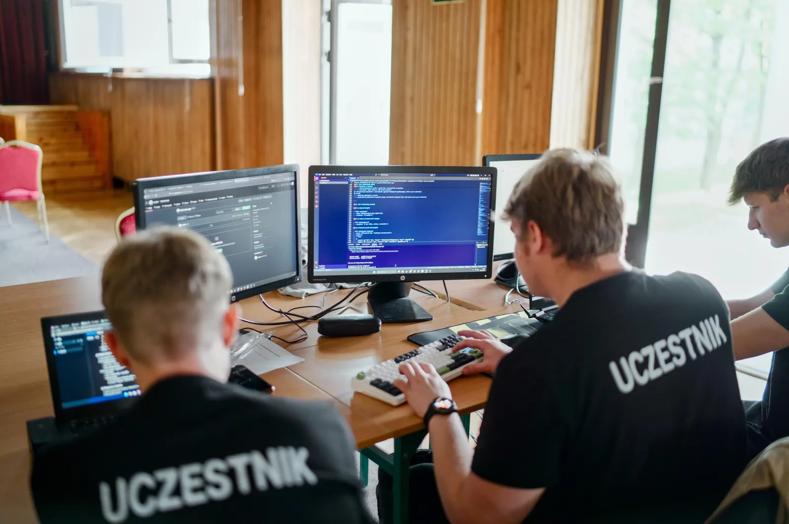 Zespół w koszulkach z napisem Uczestnik pisze kod przy kilku monitorach
